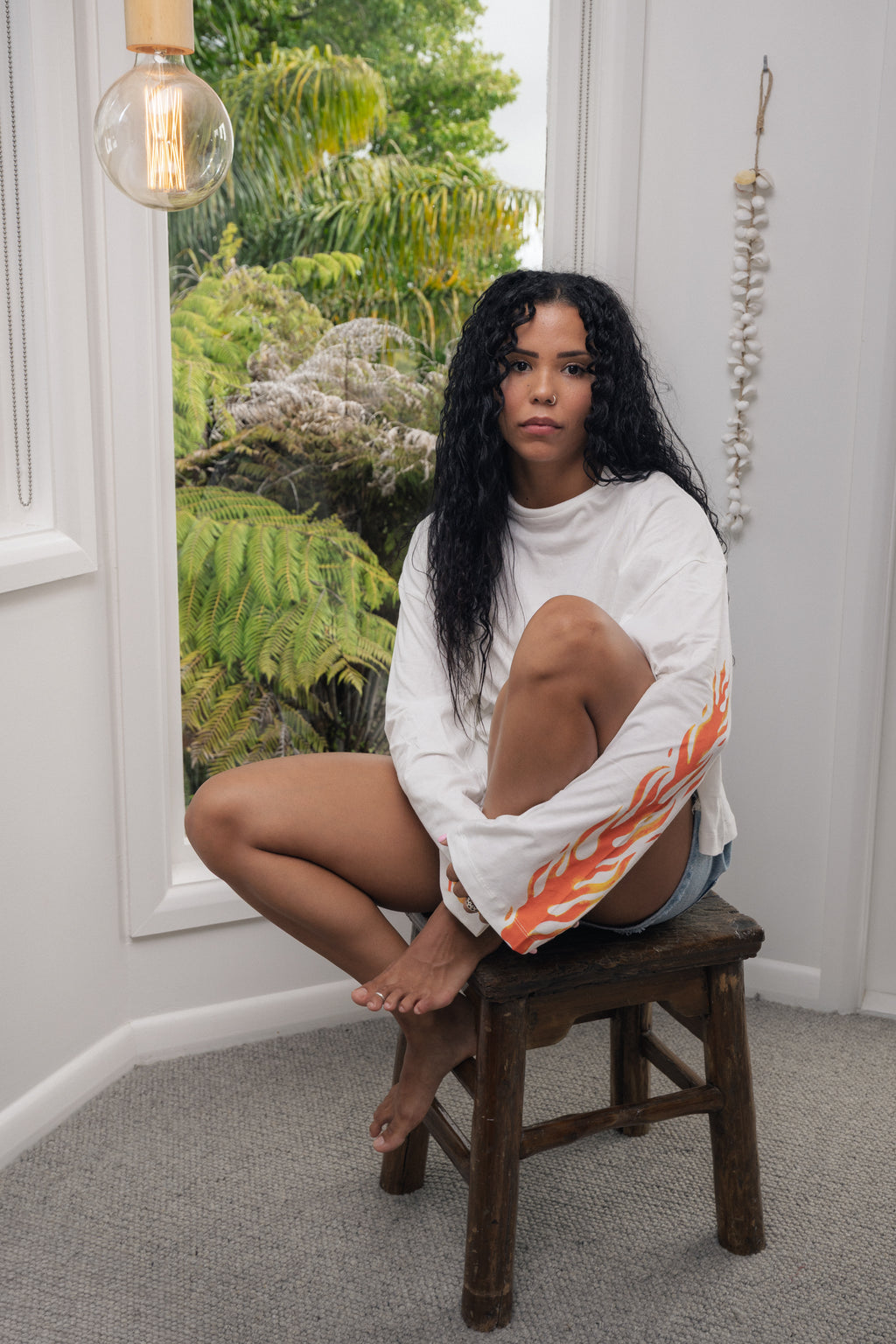 girl sitting on a stool wearing a long sleeve white t-shirt with flames on it