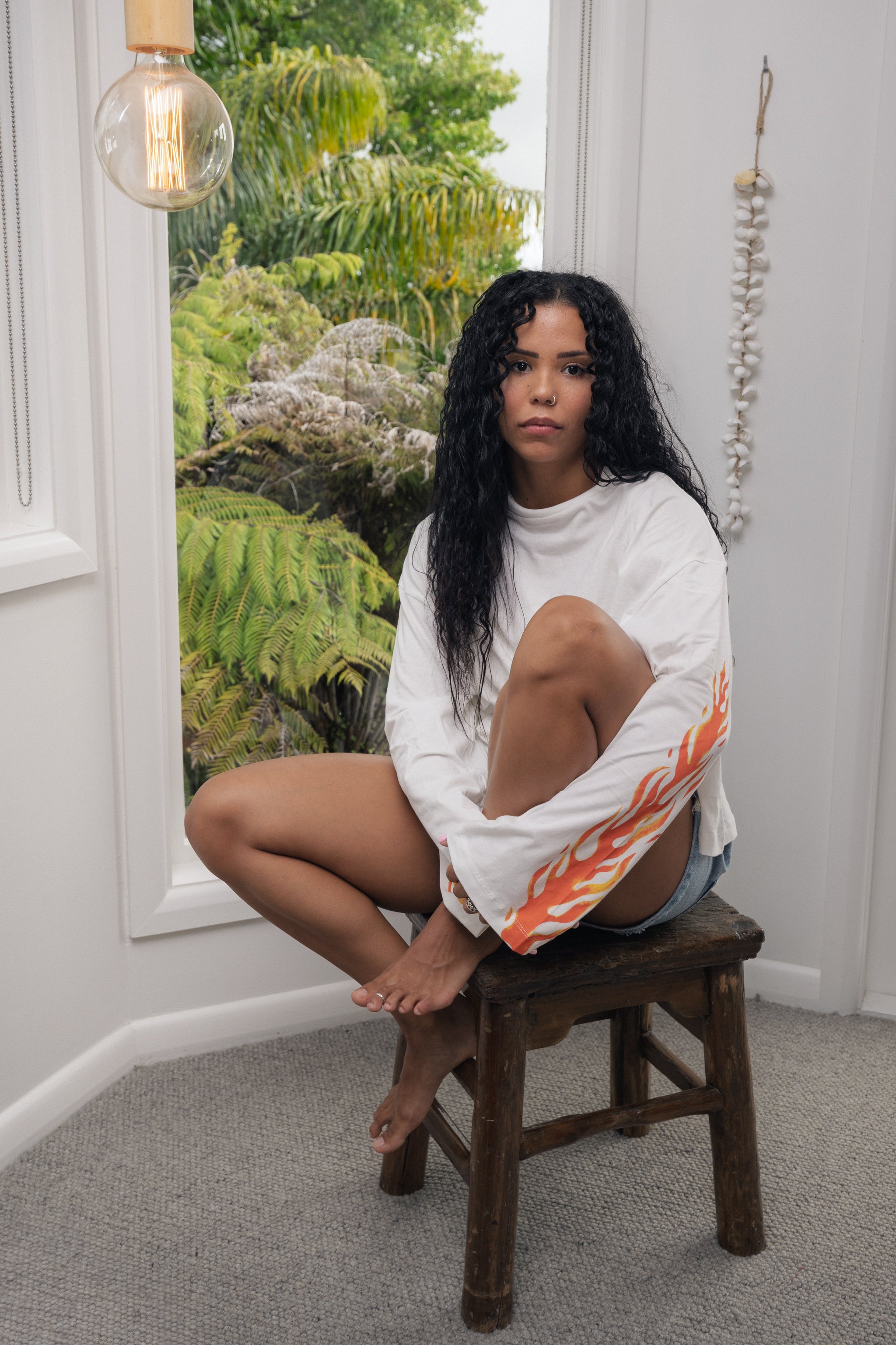 girl sitting on a stool wearing a long sleeve white t-shirt with flames on it